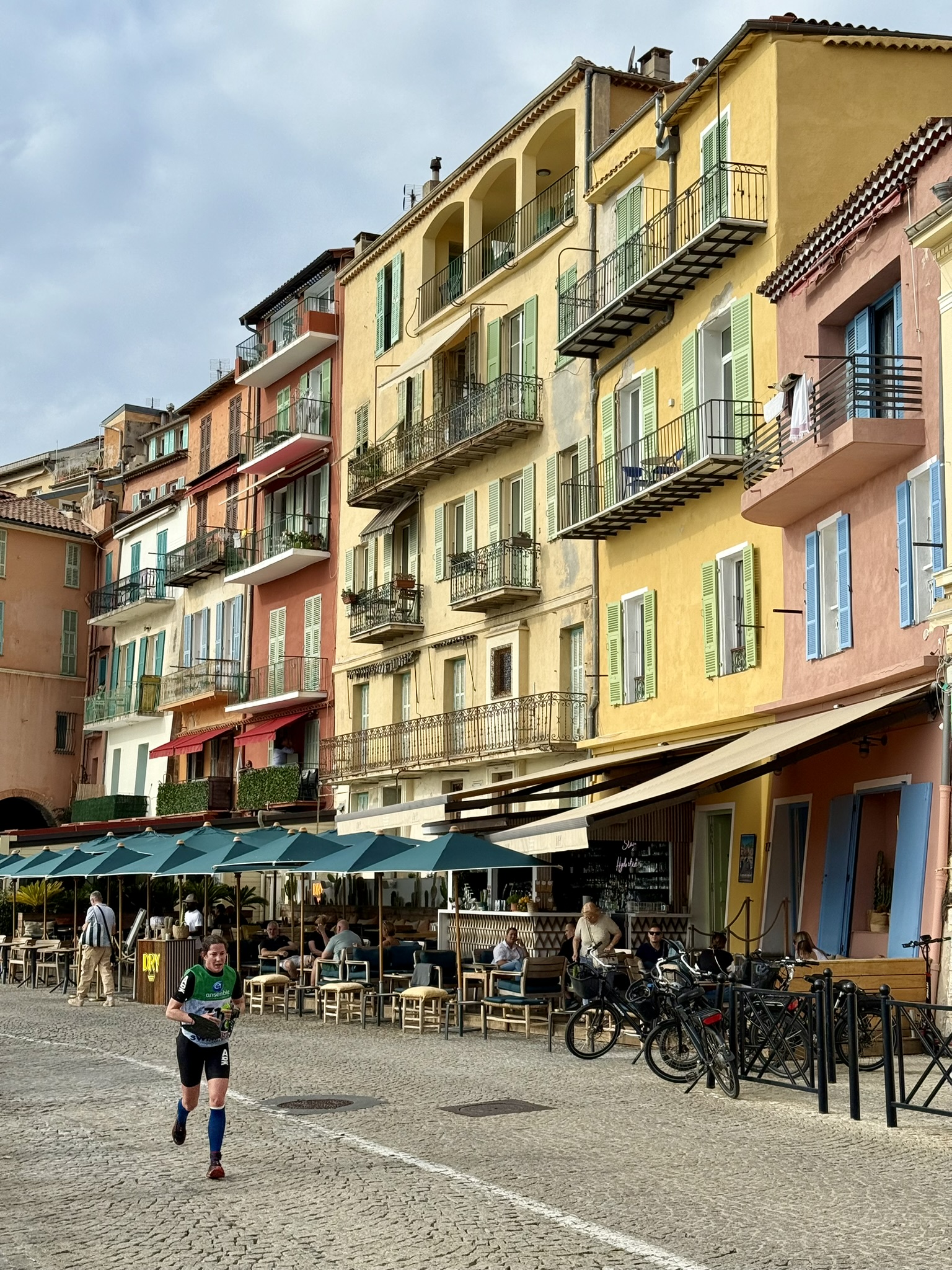 En löpare springer på en gata kantad av pastellfärgade stenhus på franska rivieran