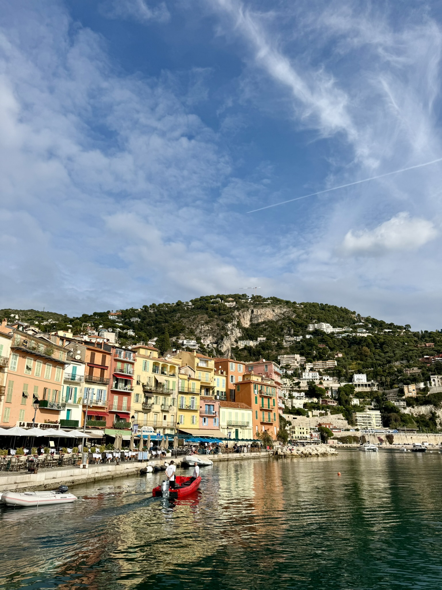 En röd båt åker på vattnet framför pittoreska färgglad stenhus i Villefranche-sur-Mer