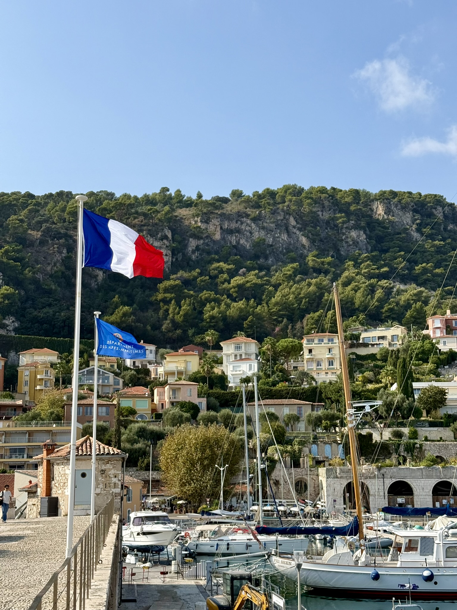 Utsikt över hamn fylld av vita båtar, franska flaggan i förgrunden